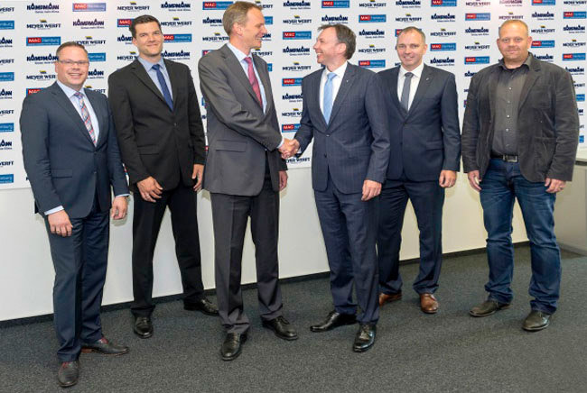 Hendrik Kampmann und Andre Gebken schütteln sich symbolisch zum Vertragsabschluss die Hände, die anderen vier Männer lächeln in die Kamera